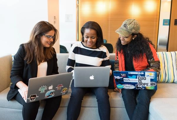 Three female colleagues in an office on their laptops smiling