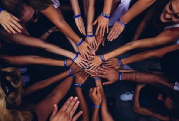 People wearing blue bracelets joining hands, Illustrating the Inclusive Culture ideal.