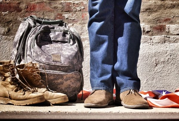 Army veteran standing beside his boots, bag, and flag
