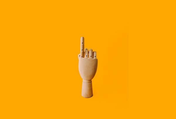 Wooden hand holding point finger up on a yellow background illustrating being first.