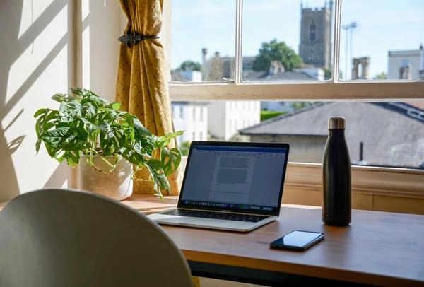 Laptop, phone, and water bottle on desk facing a window