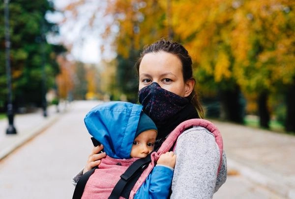 Mother wearing mask with her baby strapped to her chest at a park